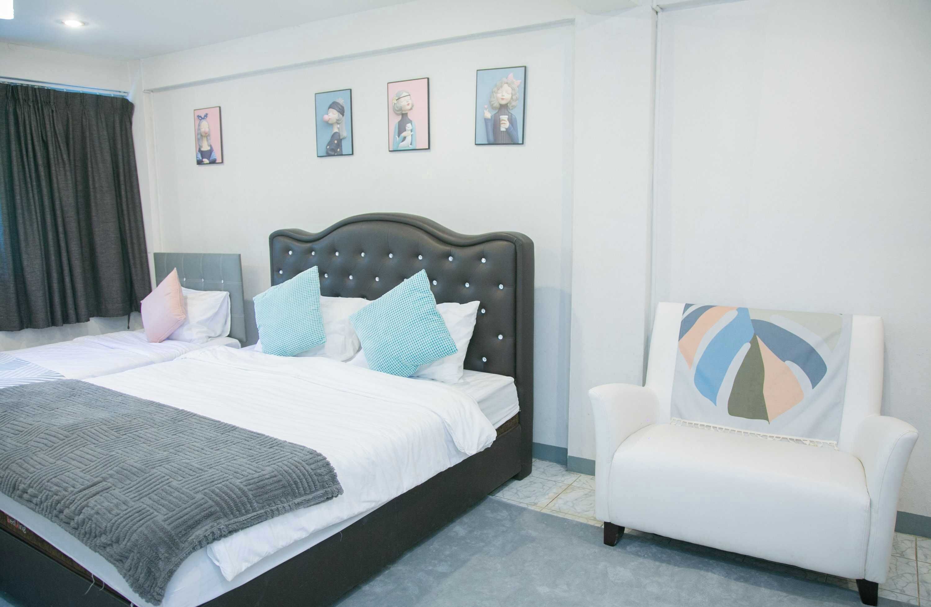 A neatly arranged bedroom with a large bed, a white armchair, and a wall with four framed pictures.