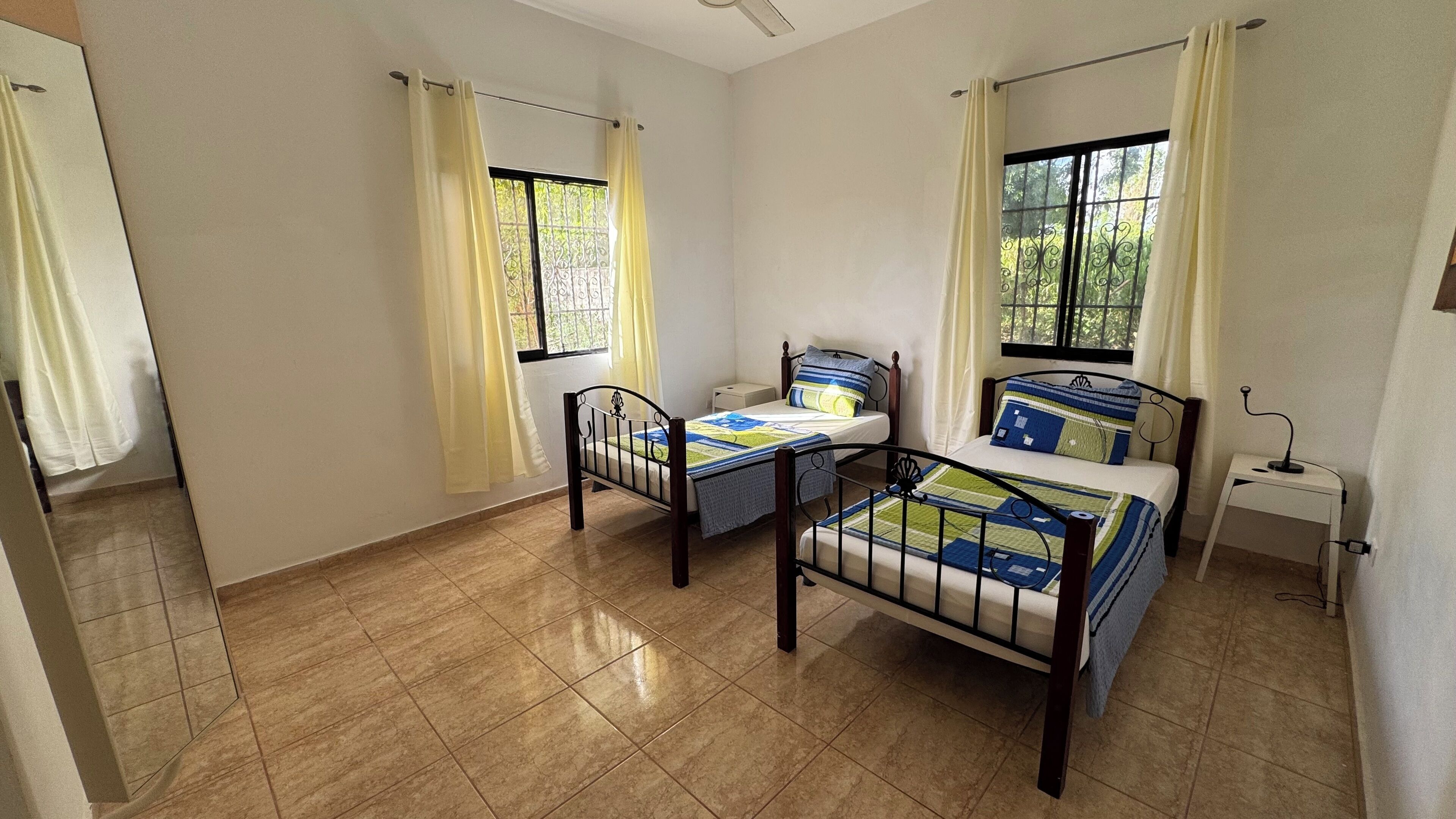 A room with two beds, a small bedside table, a nightstand, and a window with curtains.