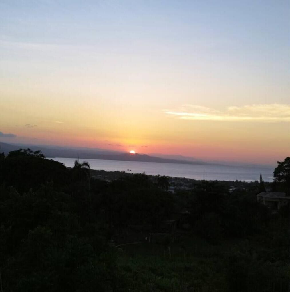 A sunset over a body of water with a silhouette of trees and a distant building.