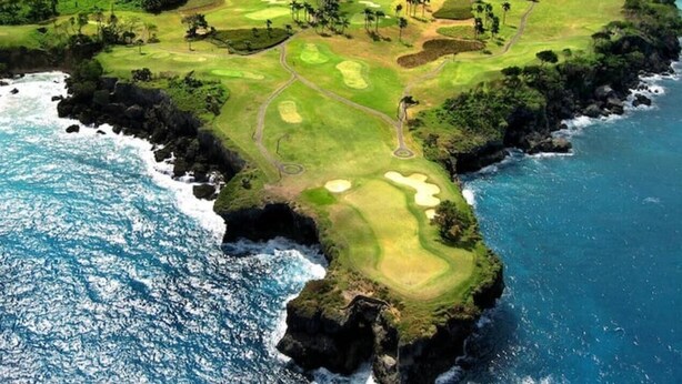 Vista aérea de un campo de golf costero con varios hoyos, cuerpos de agua y abundante vegetación.