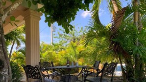 Un espacio al aire libre con una mesa y cuatro sillas, rodeado de abundante vegetación y palmeras.