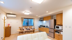 Ett kompakt bostadsutrymme med en soffa, ett matbord, stolar, en liten köksdel och ett fönster med gardiner.