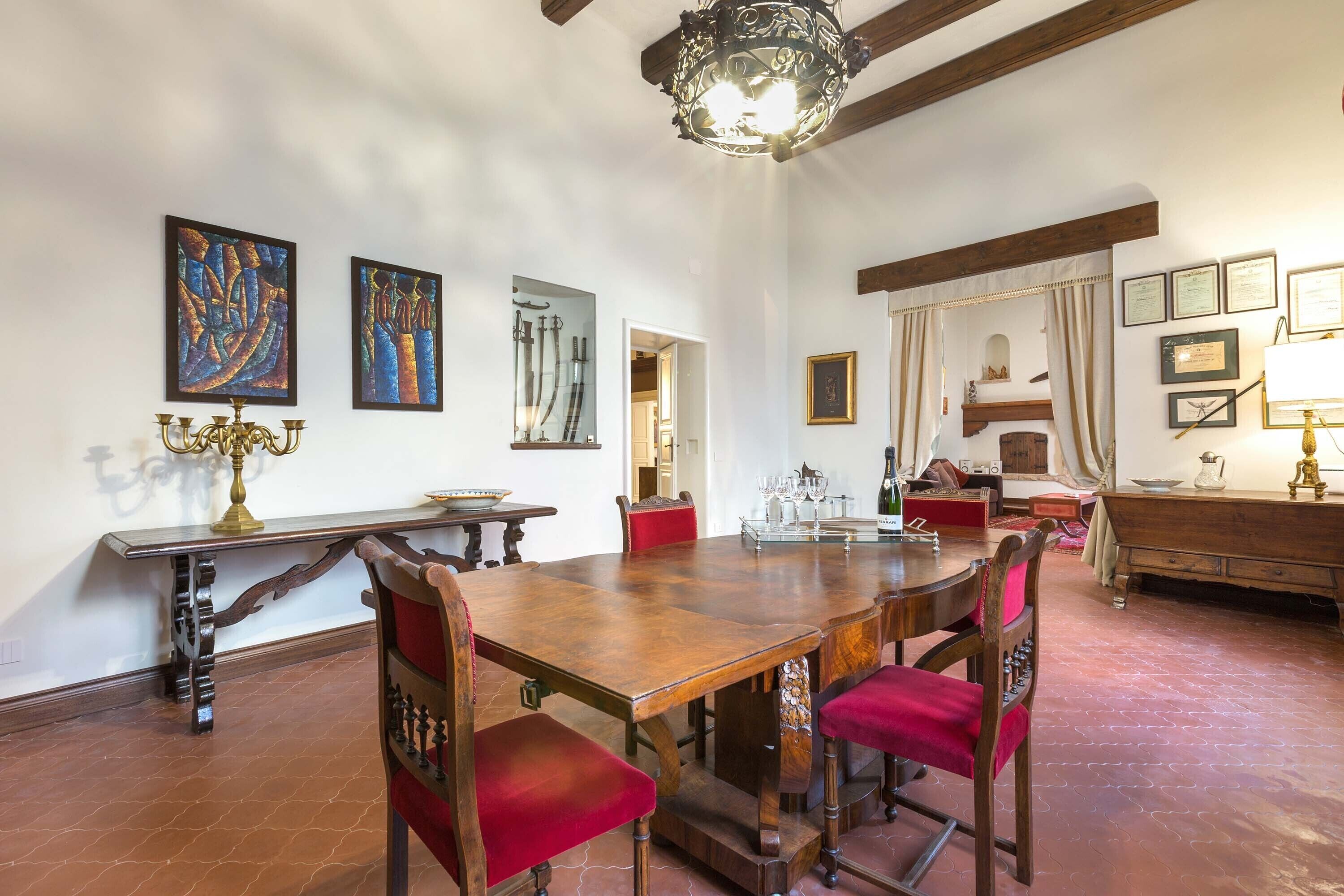 A dining area with a wooden table, red upholstered chairs, a chandelier, and artwork on the walls.