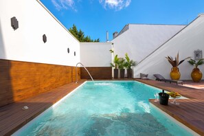 Een zwembad met een houten terras, een jacuzzi en een bar voorzien van planten en een vaas.