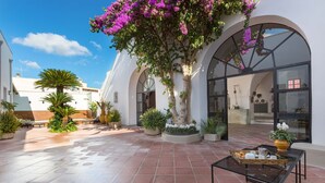 A courtyard with tiled flooring, potted plants, and a glass table with a tray.