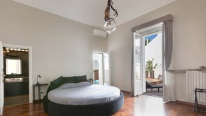 A spacious bedroom with a large bed, a modern chandelier, and a view of the outdoors through an open door.