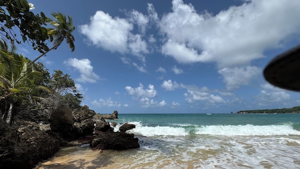 A beach with clear skies, waves, and rocky outcrops.