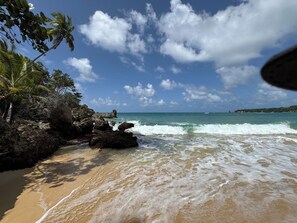 Une plage avec un ciel dégagé, des vagues et des affleurements rocheux.