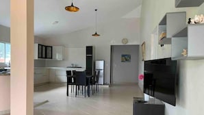 A modern kitchen with white cabinets, a dining area with a table and chairs, and a black TV stand.