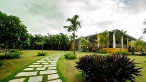 A modern building with a covered outdoor area, surrounded by well-maintained greenery and a stone pathway leading to the entrance.