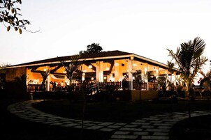 Un edificio grande con un espacio al aire libre techado, posiblemente un restaurante o salón de eventos, con un camino de piedra que conduce hacia él.