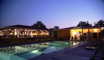 Zona de piscina con área de estar techada y un edificio con varias ventanas.