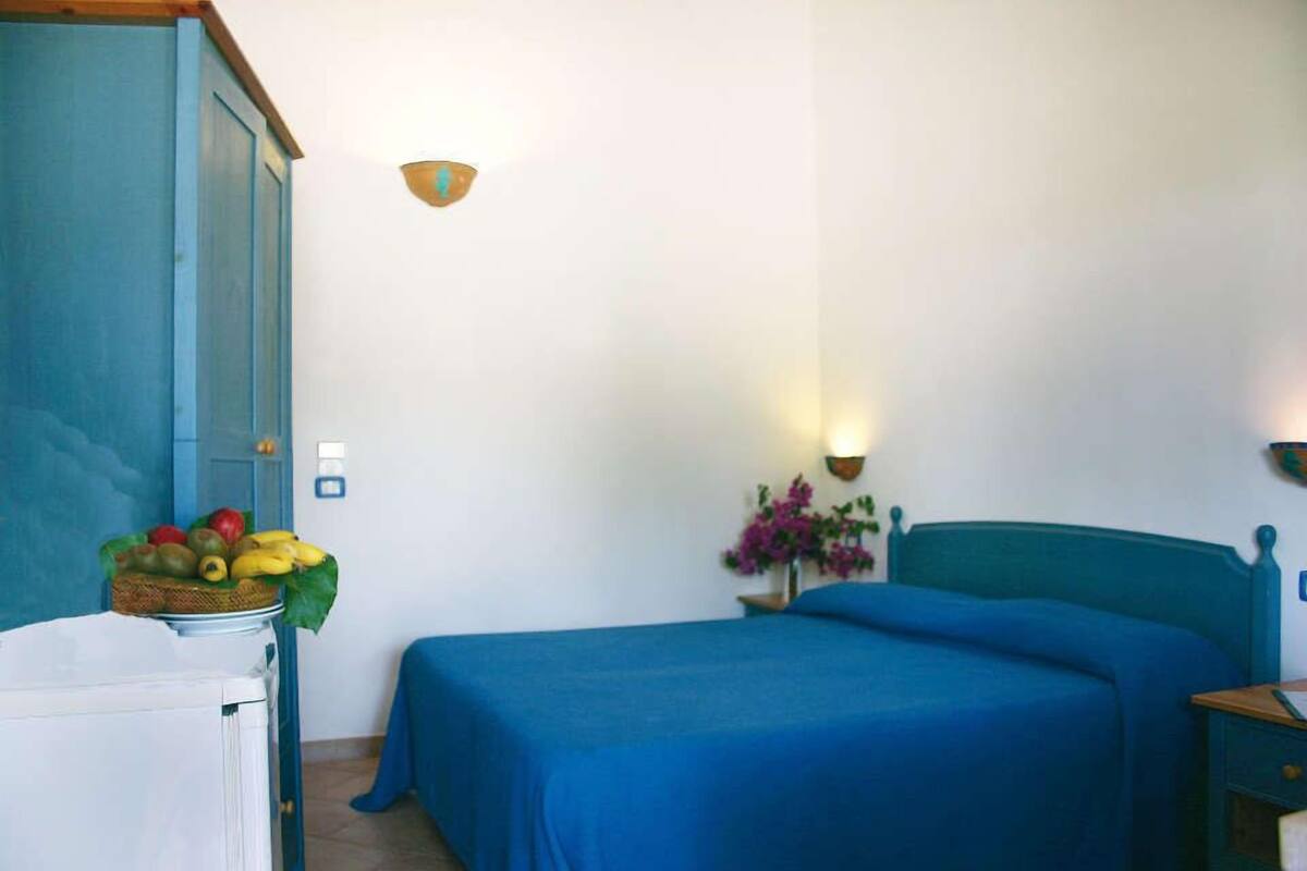 A room with a bed, a nightstand, a wall-mounted lamp, and a fruit basket on a table.