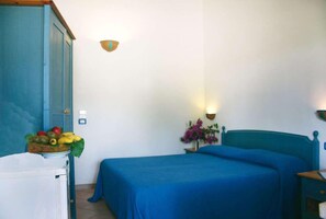 A room with a bed, a nightstand, a lamp, and a fruit basket on a table.