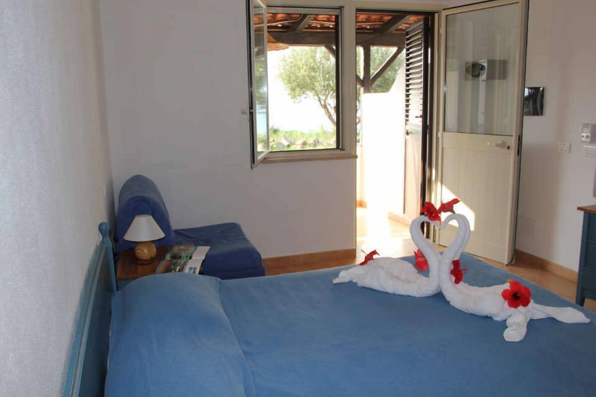 A bedroom with a bed, a nightstand, a lamp, and a window.