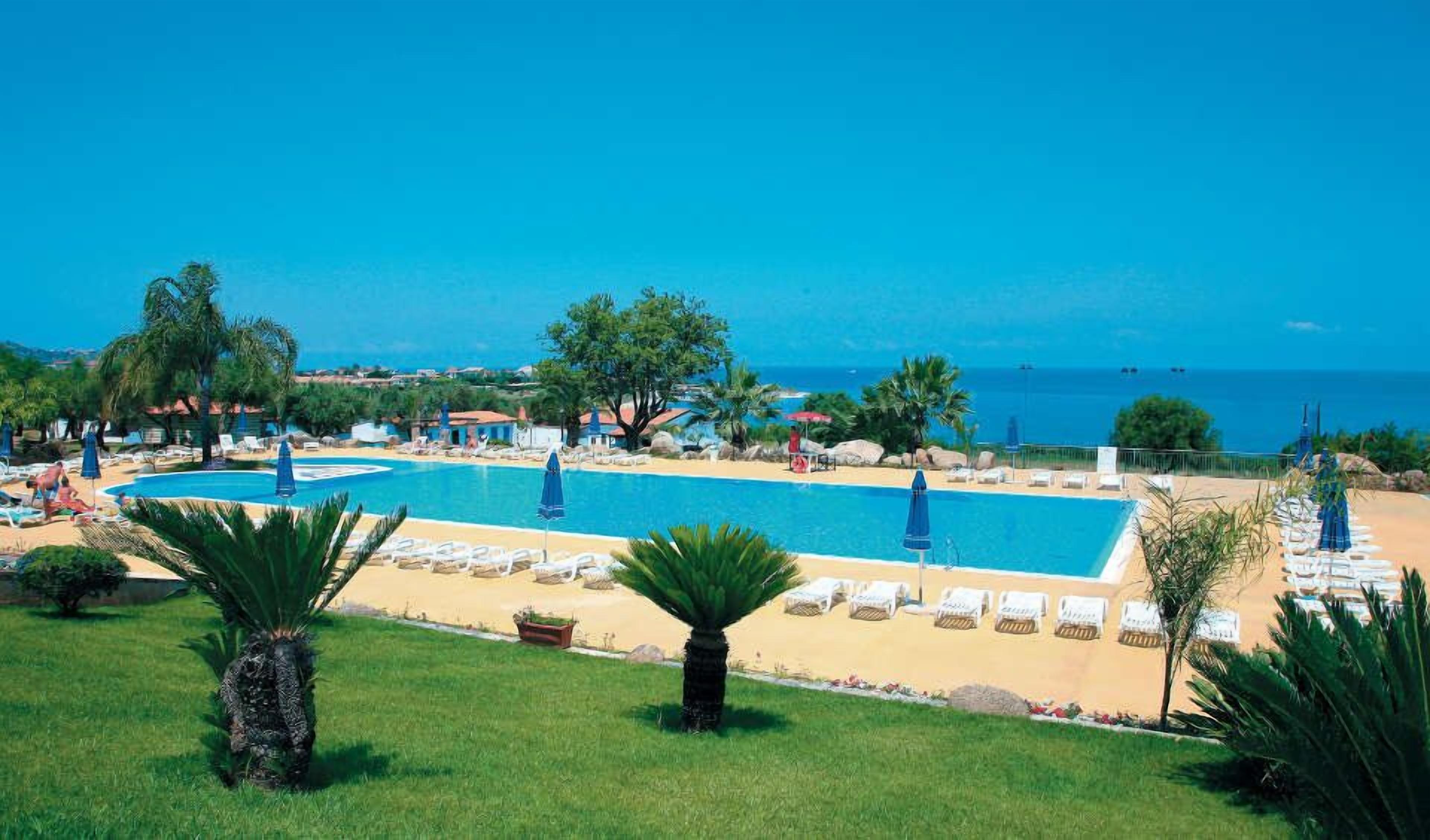 A resort with a large pool, sun loungers, and a view of the sea.