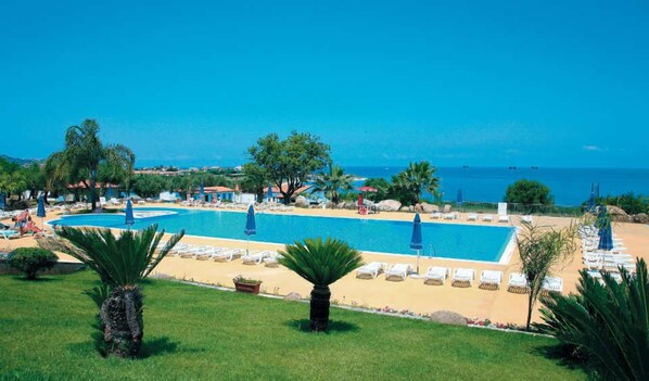 A resort with a large pool, sun loungers, and a view of the sea.