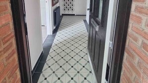 Un couloir avec un sol à motifs, une porte dotée d’un cadre sombre et un interrupteur sur le mur.