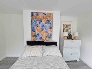 Ein Schlafzimmer mit einem Bett, einem weißen Nachttisch mit zwei Lampen und einem großen Blumenbild an der Wand.