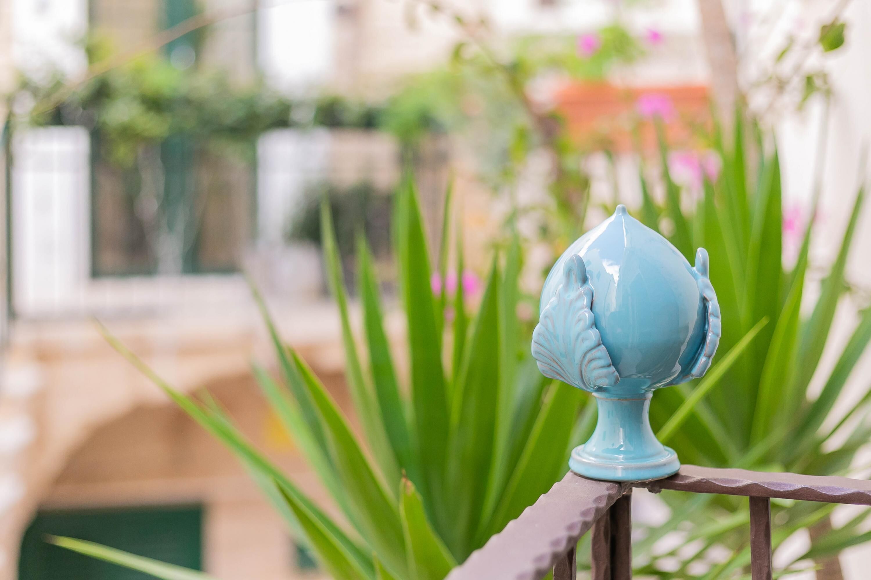 Um objeto decorativo azul numa balaustrada, com plantas verdes ao fundo.