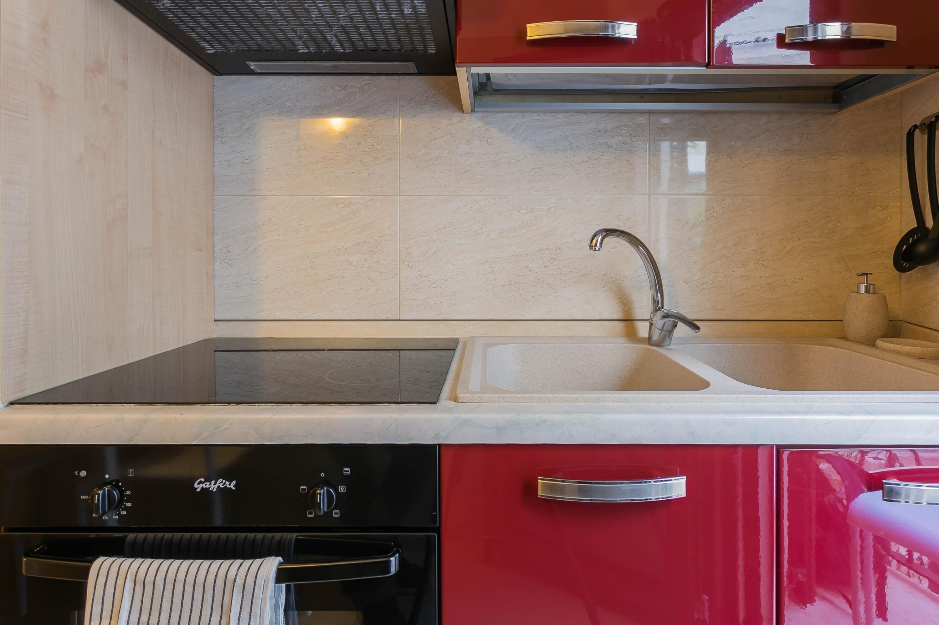 Una cocina moderna con estufa integrada, un lavamanos y armarios rojos.