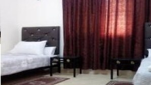 Un dormitorio con una cama, dos mesitas de noche, una ventana con cortinas y suelo alfombrado.