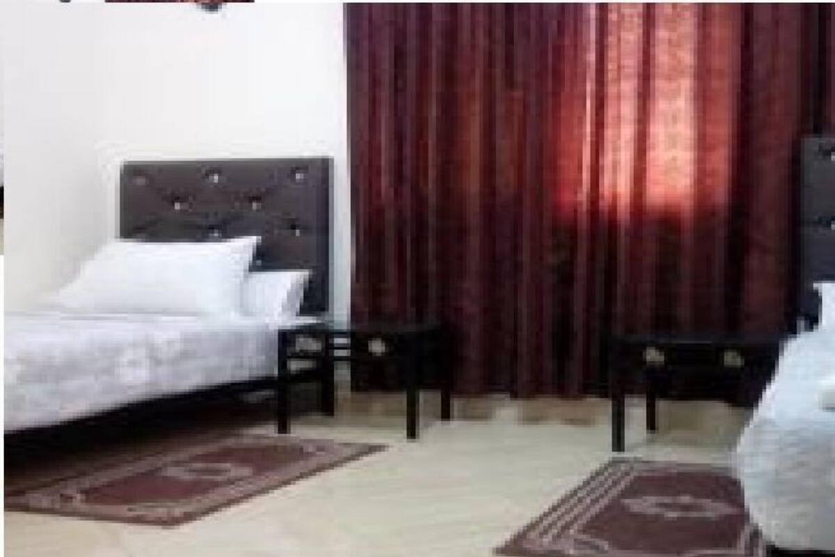 A bedroom with a bed, two nightstands, a window with curtains, and a carpeted floor.