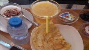 Bandeja de desayuno con una porción de tortilla, un vaso de zumo de naranja, una botella de agua y un pequeño recipiente de yogur.