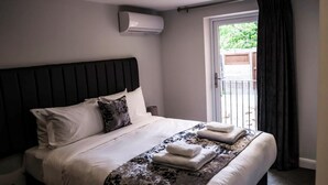 A modern hotel room with a large bed, a headboard, a window with curtains, and an air conditioning unit. - Anelli Hotel (Southport)
