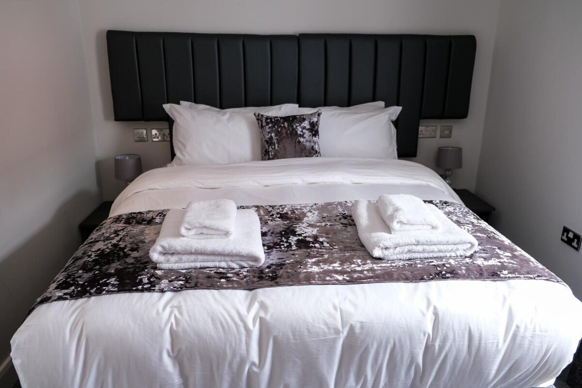 Ett hotellrum med en säng, kuddar, en sänggavel, sänglampor och handdukar.