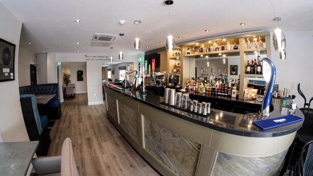 A bar area with a long counter, multiple taps, and a variety of bottles and glasses. - Anelli Hotel (Southport)