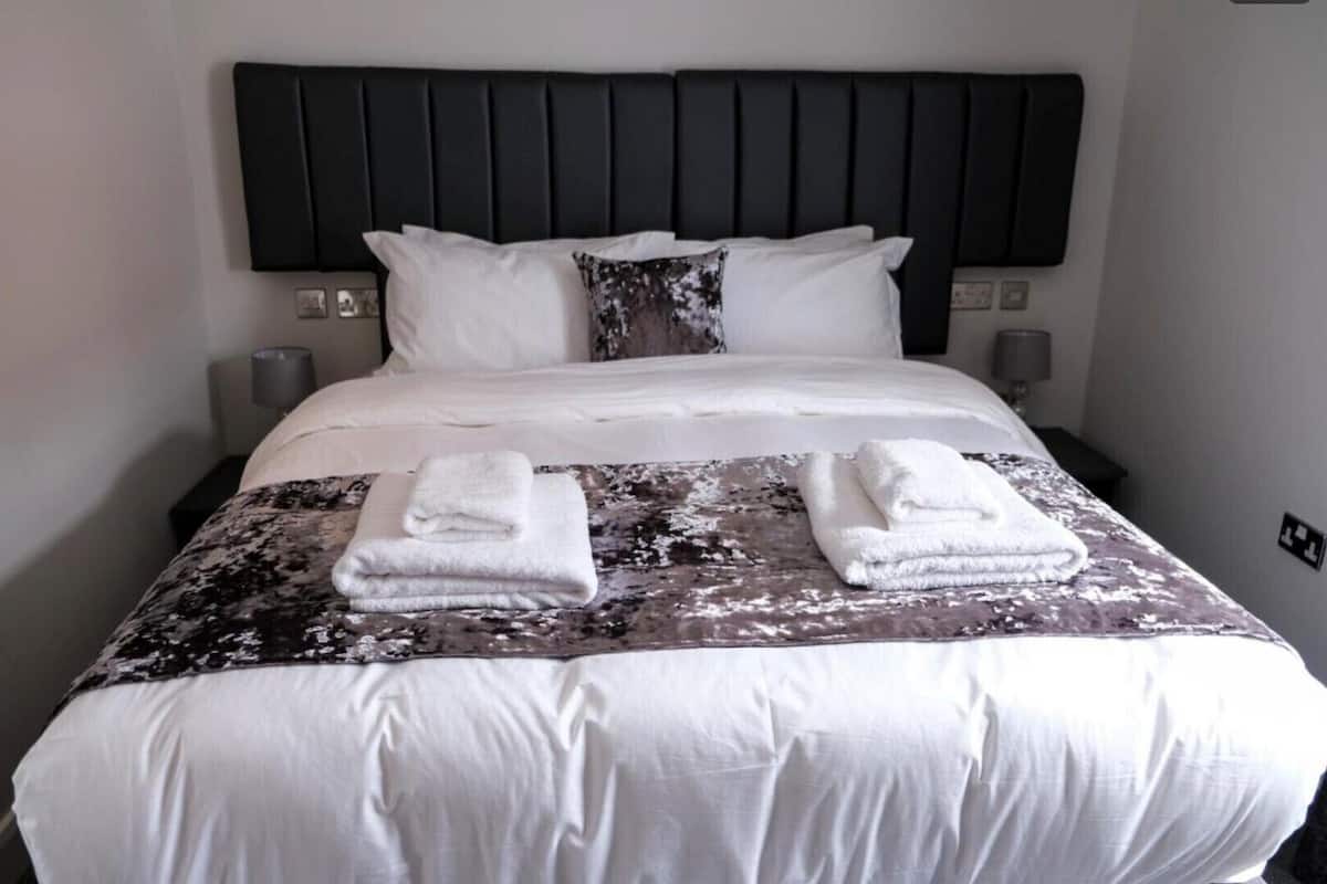 A hotel room with a large bed, white linens, a dark headboard, and two bedside lamps.