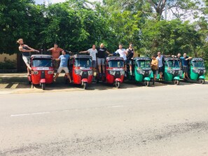 Eine Gruppe von Menschen posiert mit Auto-Rikschas auf einer Straße.
