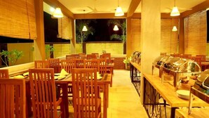 Ein Restaurant mit Holztischen und -stühlen, einem Buffetbereich und großen Fenstern mit Blick ins Freie.