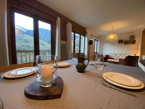 A dining table set with plates, glasses, and a candle centerpiece, with a view of a mountainous landscape through large windows. - Family Chalet for 8/9, 5 mins to Village Center, Mountain Views, WiFi (Arêches-Beaufort)