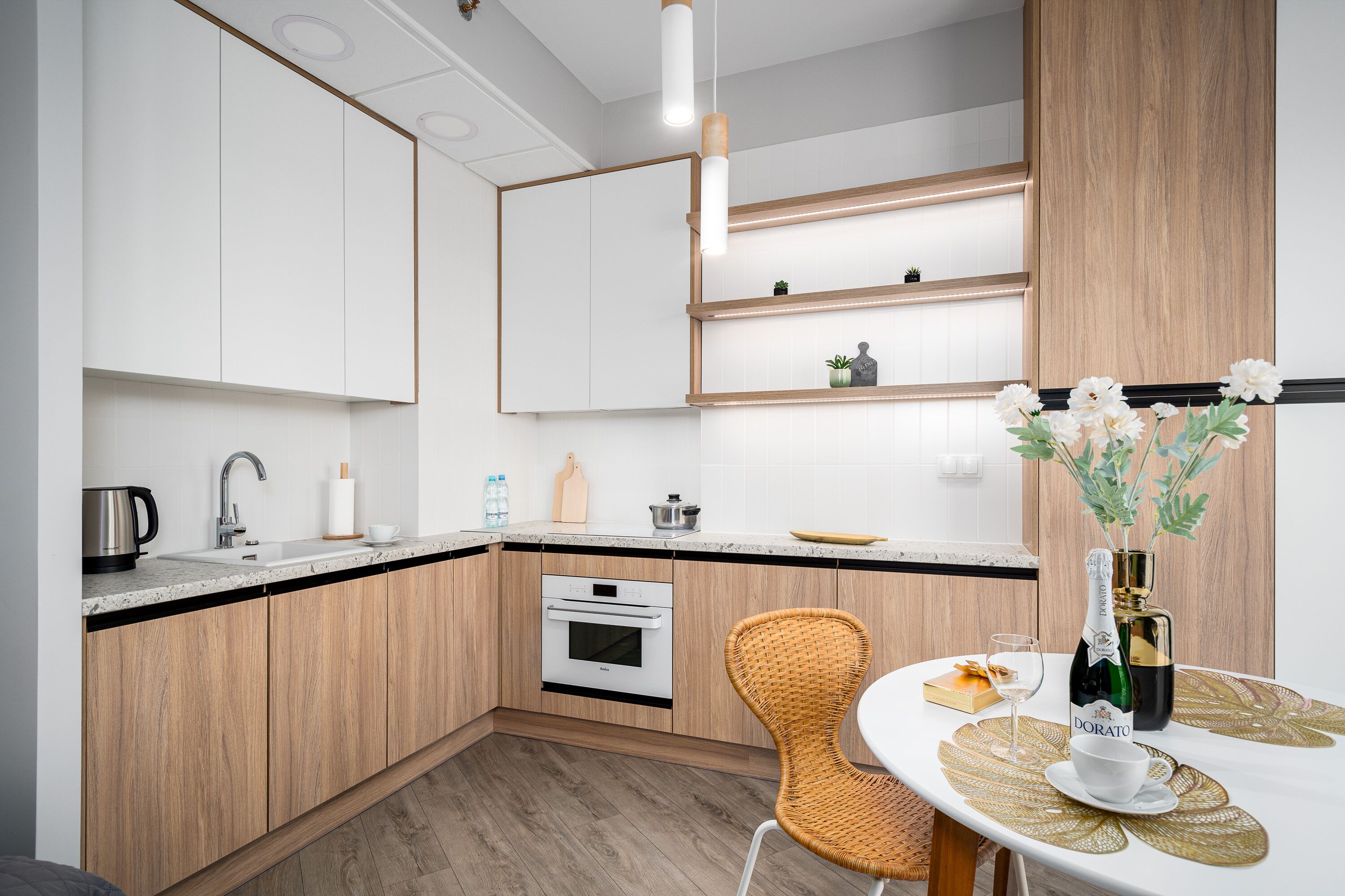 A modern kitchen with wooden cabinets, a built-in oven, a sink, and a dining area with a table and chairs.