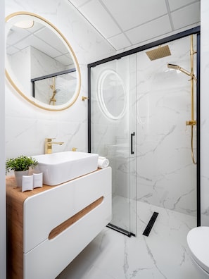 Ein modernes Badezimmer mit einem weißen Marmorwaschbecken, goldenen Armaturen und einer Duschkabine.
