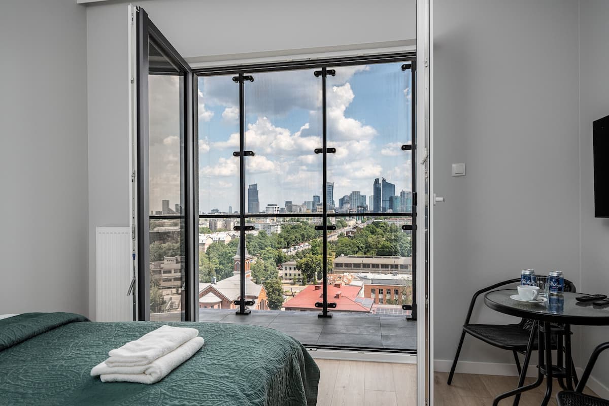 Een kamer met een bed, een tafel met drankjes en een uitzicht op een stadsbeeld door een groot raam.