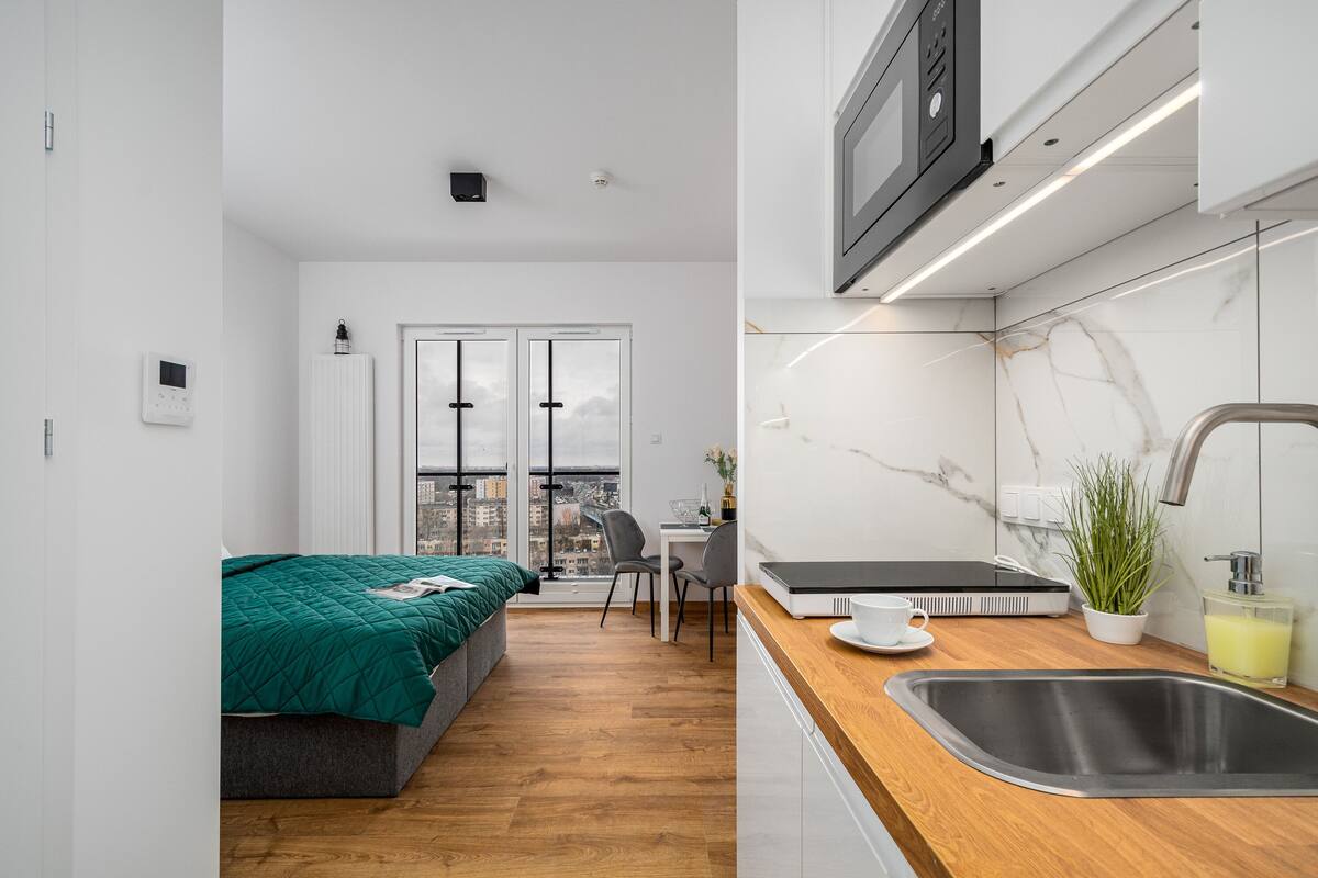 Een modern appartement met een bed, een bureau en een keukenhoek met een spoelbak en een magnetron.