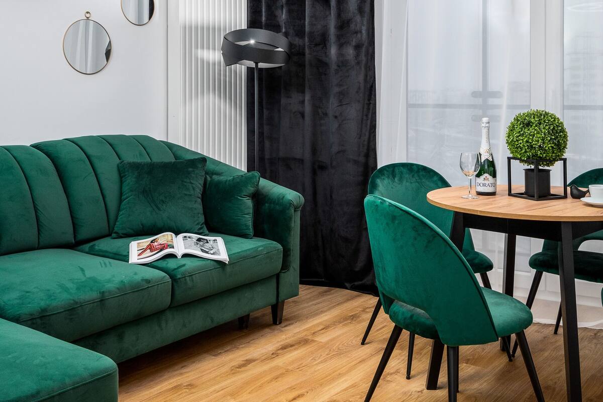 Een moderne woonkamer met een groene bank, een ronde houten tafel en groene stoelen.