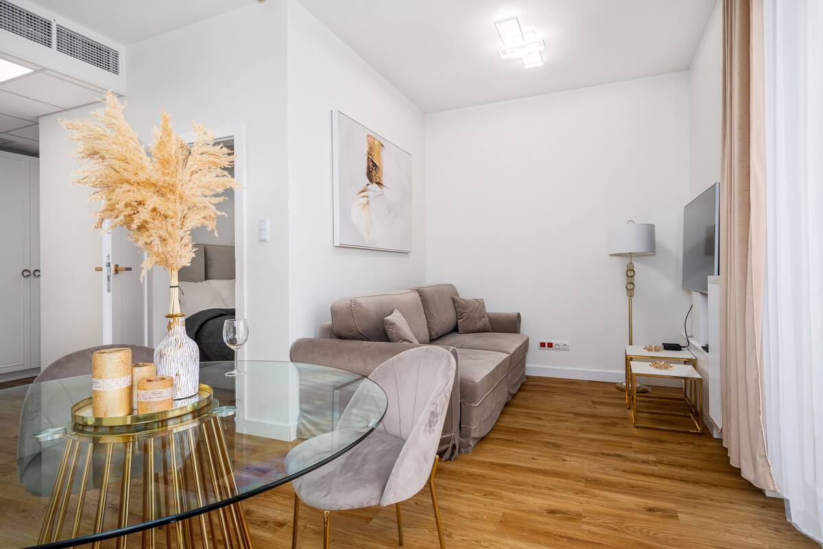 Een moderne woonkamer met een glazen salontafel, een beige bank en een televisie op een standaard.