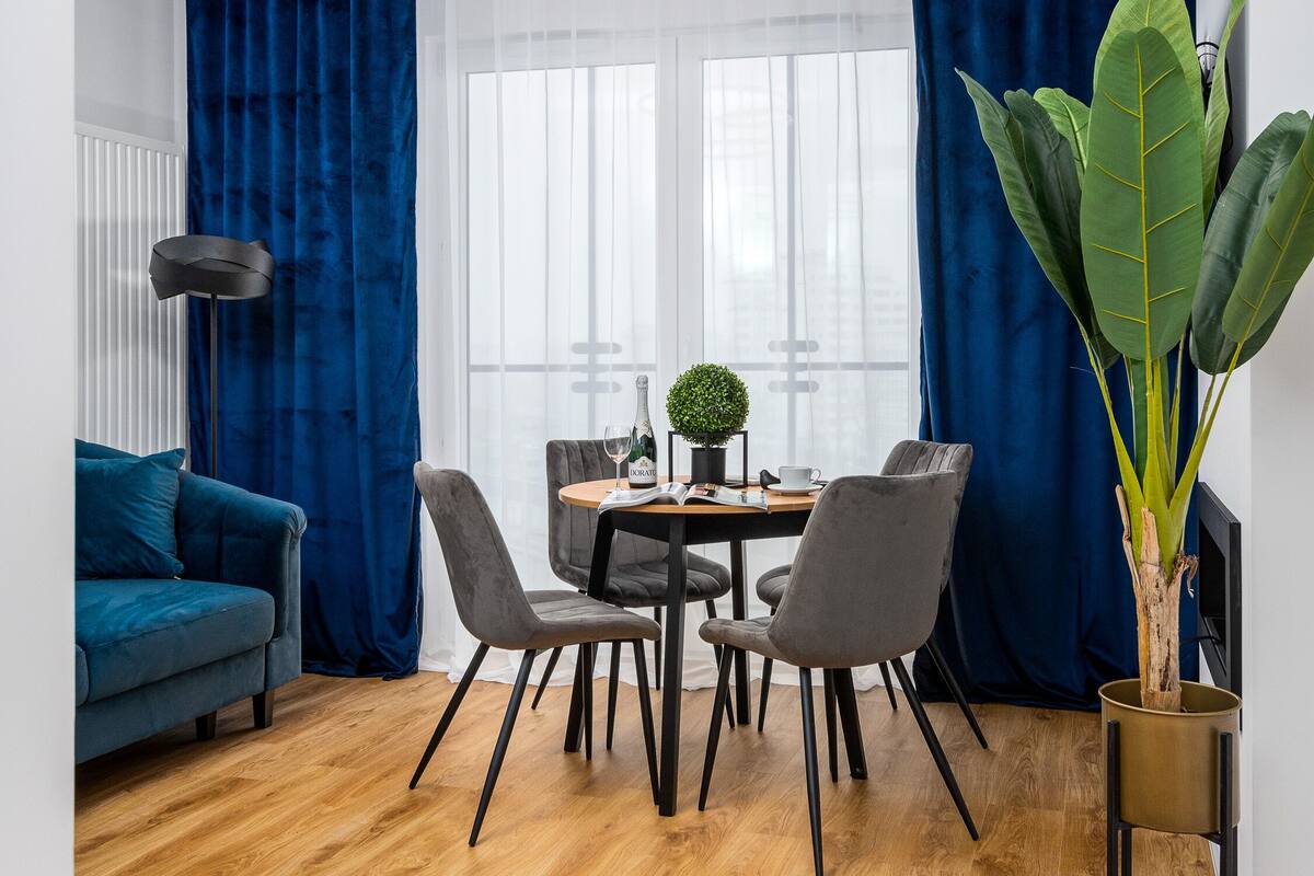 Een moderne eetruimte met een ronde tafel, vier stoelen, een bloempot en een fles wijn.