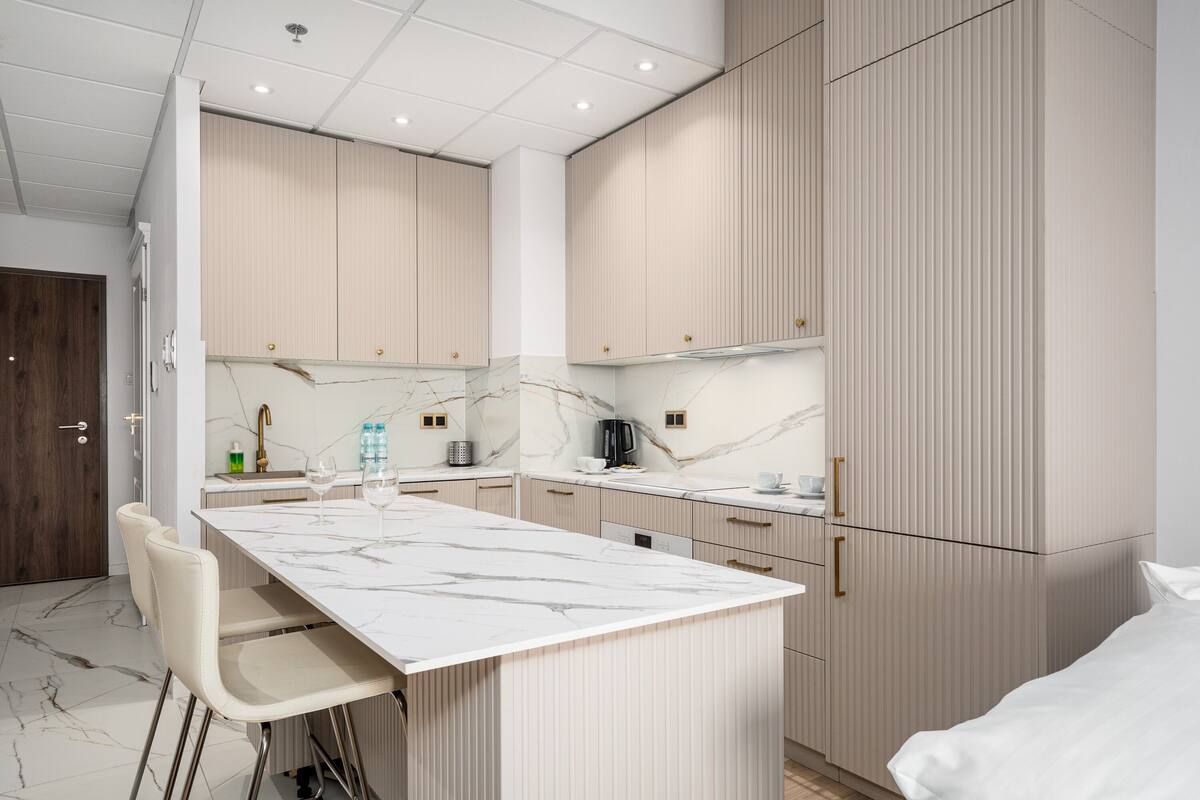 Een moderne keuken met een marmeren aanrechtblad, witte kastjes en een inbouw eiland met barstoelen.
