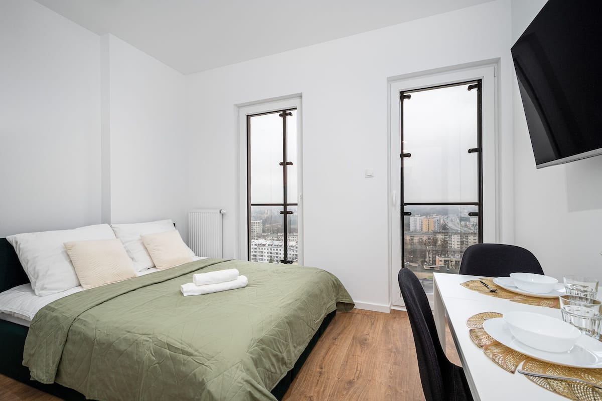 Een moderne hotelkamer met een bed, een eettafel gedekt met borden en glazen, en grote ramen met uitzicht op de stad.