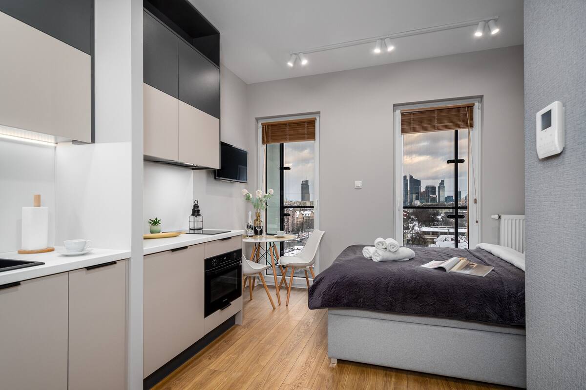 Een moderne hotelkamer met een keuken, eethoek en een groot bed met uitzicht over de stad.