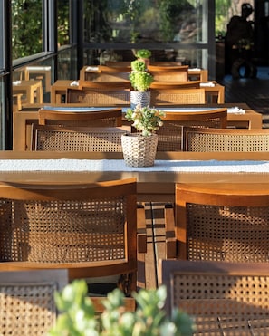 A restaurant with wooden tables and chairs, a woven planter with plants, and large windows.
