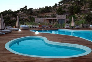 Un área de piscina con dos piscinas, sillas de descanso y sombrillas.