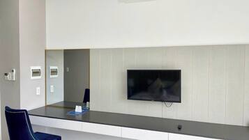 A hotel reception area with a flat-screen TV mounted on the wall, a desk with a chair, and an air conditioning unit above.