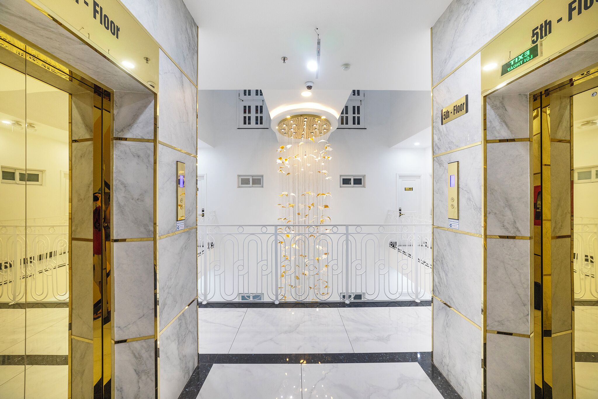 Eine moderne Hotelhalle mit Marmorböden, einem zentralen Kronleuchter und Aufzugtüren mit der Aufschrift '5. Etage'.