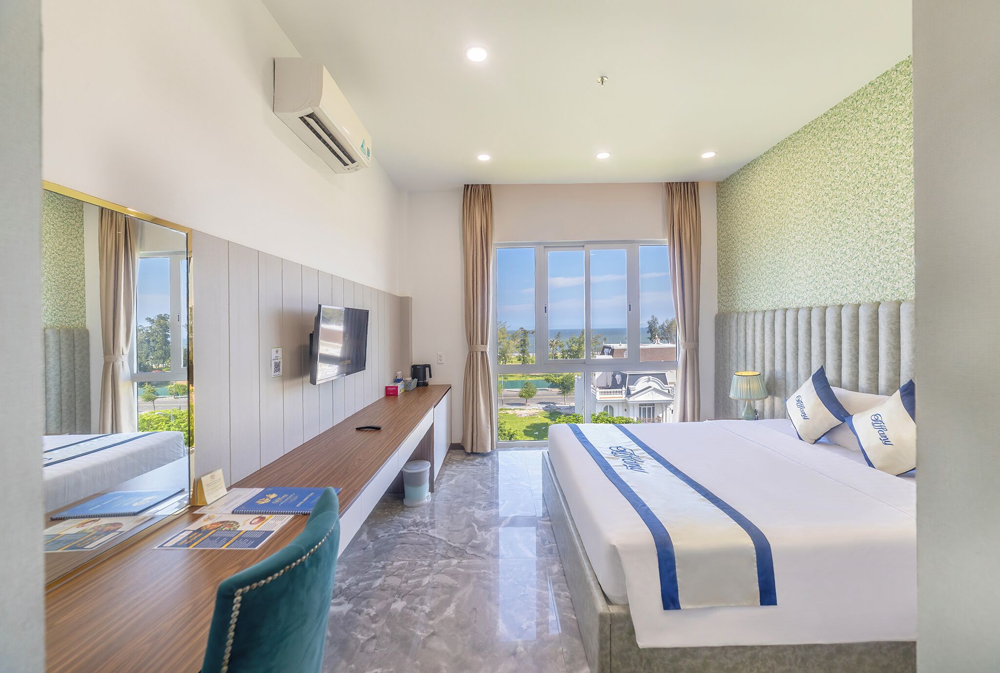 A hotel room with a bed, a desk, a chair, a TV, and a window with a view of the outside.